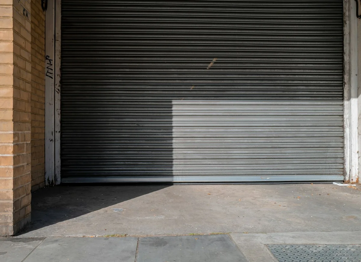 Gray rolling steel door closed in a brick wall, showing the interlocking steel slat curtain